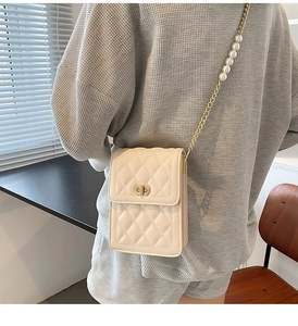 Detail of cream quilted phone bag featuring elegant pearl and gold chain strap