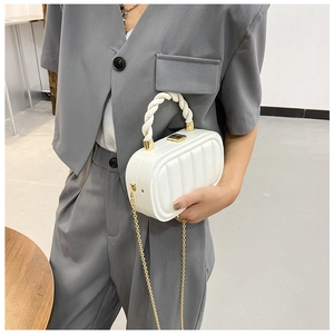 Detail of white textured shell handbag featuring woven handle and gold chain strap