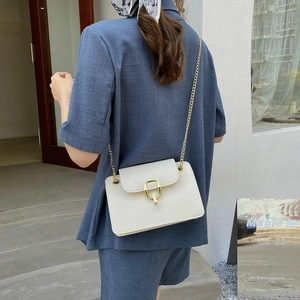 Chic white leather crossbody bag with gold oval lock and chain strap on a stylish model