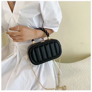 Detail of black quilted handbag with golden chain strap and twisted handle on white dress
