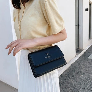 Chic black faux leather crossbody bag with gold chain strap and deer logo on a model