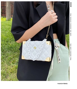 Close-up of white quilted box bag featuring gold hardware and acrylic chain details