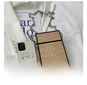 Detail view of wood grain box bag with chain strap next to a phone for size reference
