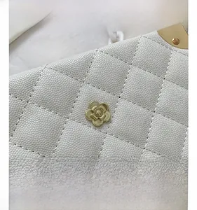 Detail of white lychee leather bag featuring gold flower hardware and acrylic chain link
