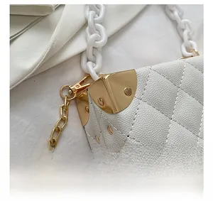 Detail of white quilted crossbody bag with gold corner guards and acrylic chain strap