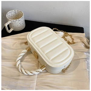 Detail of white quilted handbag with woven gold-tone handle and elegant metallic chain