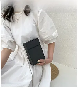 Detail of a black wood grain box bag with silver chain strap worn over a white dress