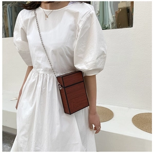 Detailed view of a brown wood pattern box bag with silver chain worn on a white dress