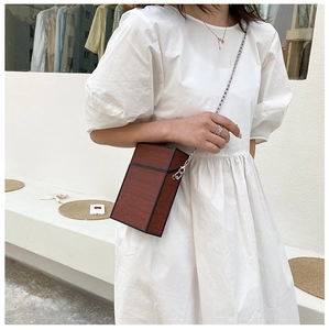 Detail of wooden texture box bag with silver chain strap worn by a model in white dress