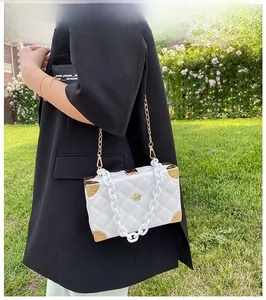 Close-up of white quilted box bag with gold flower logo and acrylic chain straps