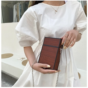 Detailed view of women's wooden texture box bag with silver chain and white dress styling