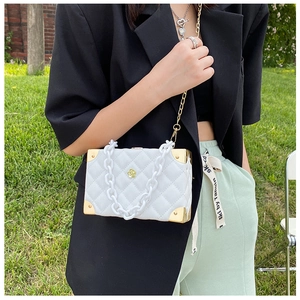 Detailed view of white quilted box bag with acrylic chain and gold camellia ornament