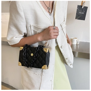 Detail of black quilted box bag with gold metal corners and acrylic chain strap