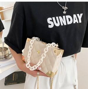 Quilted beige box bag detail featuring gold corner guards and acrylic chain handle