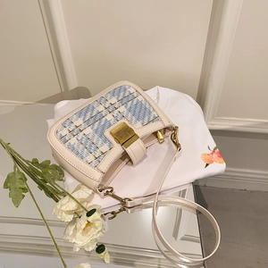 Blue woven shoulder bag with white leather trim and gold metal buckle on a white T-shirt