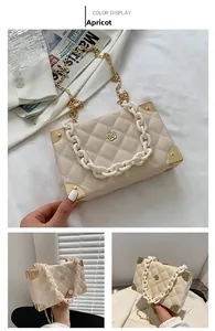 Detail of beige quilted box bag featuring gold floral clasp and metal corner accents