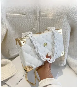 Close-up of a white quilted box bag with gold metal edges and acrylic chain details
