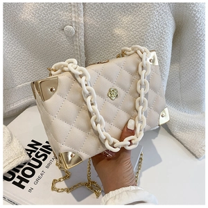 Close-up of cream quilted bag with golden camellia logo and acrylic chain detail