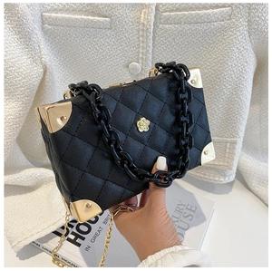 Close-up of black quilted box bag with acrylic chain handle and gold camellia logo