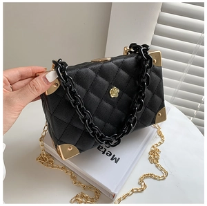 Detail of black quilted box bag with gold flower logo and metal corner guards