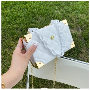 Detail of white quilted crossbody box bag with gold floral clasp and metal corner guards