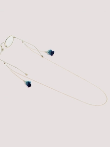 Detailed shot of golden eyewear chain with gradient blue silk tassels on pink background