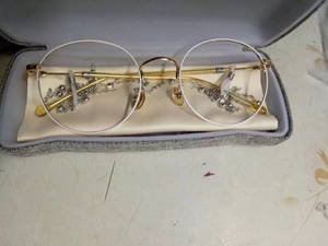 Detail of round white frame glasses with gold metal arms and a beaded silver chain