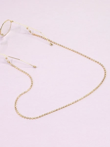 Close-up of golden eyeglass chain with sparkling rhinestones on light purple surface