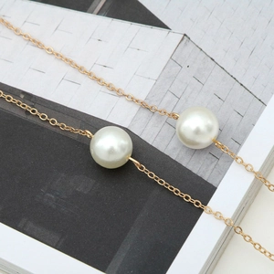 Minimalist double gold chains necklace featuring two elegant large white pearls on a magazine