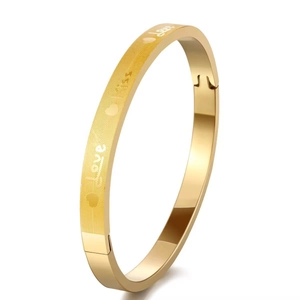 Detail of gold oval bangle with brushed finish and engraved love kiss patterns