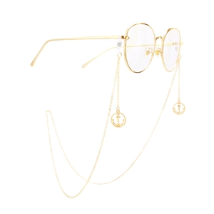Lunettes rondes dorées avec chaîne en métal élégante et pendentifs ancre sur fond blanc
