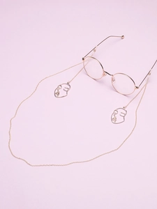 Detail of gold metal glasses chain with abstract face charms on a purple background