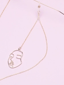 Detail of golden glasses chain featuring a minimalist abstract face outline pendant