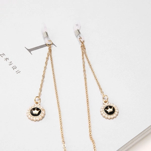 Chaîne de lunettes dorée avec pendentif couronne et perles sur un livre blanc