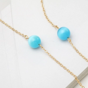 Golden eyewear chain with blue cat-eye beads on a textured white surface background