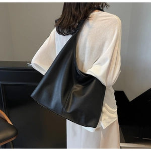 Close-up of black pebbled leather tote bag with minimalist crescent shape on shoulder