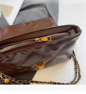 Detail of dark brown quilted leather bag with golden zipper and metal chain strap
