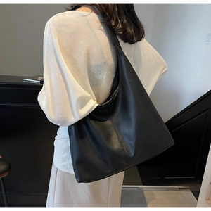 Close-up of a large black tote bag in soft pebble leather worn by a model in a room