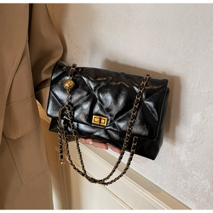 Detail of black quilted chain bag with gold buckle on a model wearing a khaki trench coat