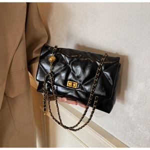 Close-up of black quilted shoulder bag with gold chain strap and adjustable ball