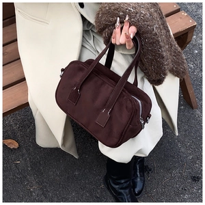 Detail of dark brown matte suede Boston bag with silver zipper and handle held by model