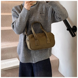 Detail view of olive green suede Boston bag worn on shoulder in minimalist setting
