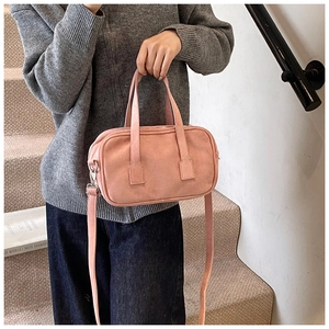 Detailed view of pink matte suede crossbody bag held by a model in casual grey knitwear