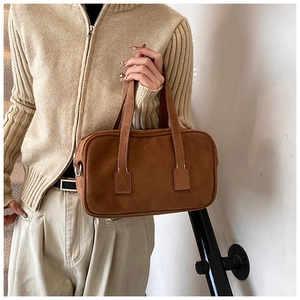 Brown suede Boston bag detail with stitching and double handles held by model