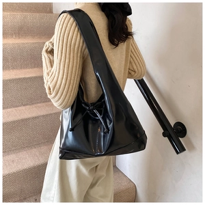 Close-up of the glossy black faux leather shoulder bag with chic drawstring bow detail
