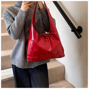 Close-up of bright red patent leather hobo bag with decorative bow and glossy finish