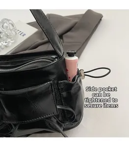Detail of adjustable side drawstring pocket on black glossy leather shoulder bag