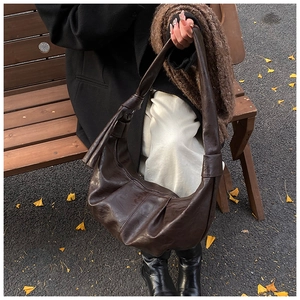 Close-up of dark brown crescent hobo bag with knotted strap on wooden bench