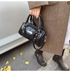 Close-up of glossy black cylinder bag with silver metal zipper and buckles in autumn setting