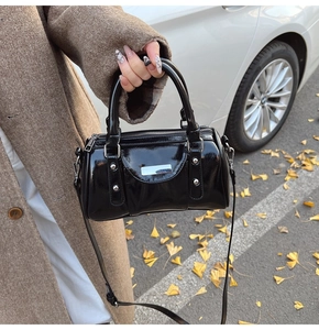 Detail of black patent leather cylinder bag with silver studs and adjustable strap